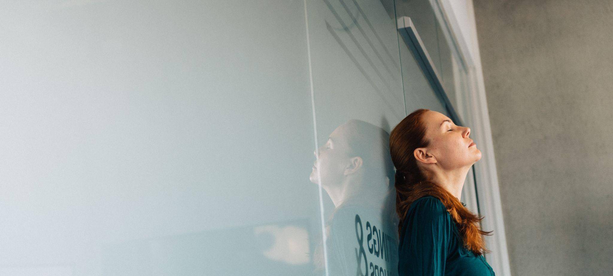 Eine junge Frau lehnt nachdenklich an einer Glaswand